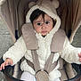 Ayla participe au concours pour gagner de l'argent avec cette photo : baby, child, stroller, hoodie, white_clothing, bear_ears, cute, infant, seatbelt, outdoor, pavement, curious_expression, warm_clothing, hands, person, face, portrait, sitting, bundle, winter
