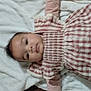 baby, infant, child, face, eyes, cheeks, gingham_dress, dress, blanket, towel, lying_down, indoors, wooden_floor, portrait, cute, smile, cozy, fabric, bedding, human