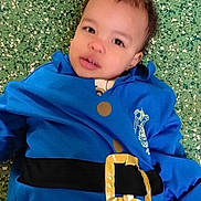 Hayden participe au concours pour gagner de l'argent avec cette photo : child, toddler, face, eyes, blue_jacket, belt, gold_buckle, green_floor, speckled_floor, socks, pants, lying_down, indoor, portrait, curly_hair, casual_clothing, expression, looking_up, closeup, skin