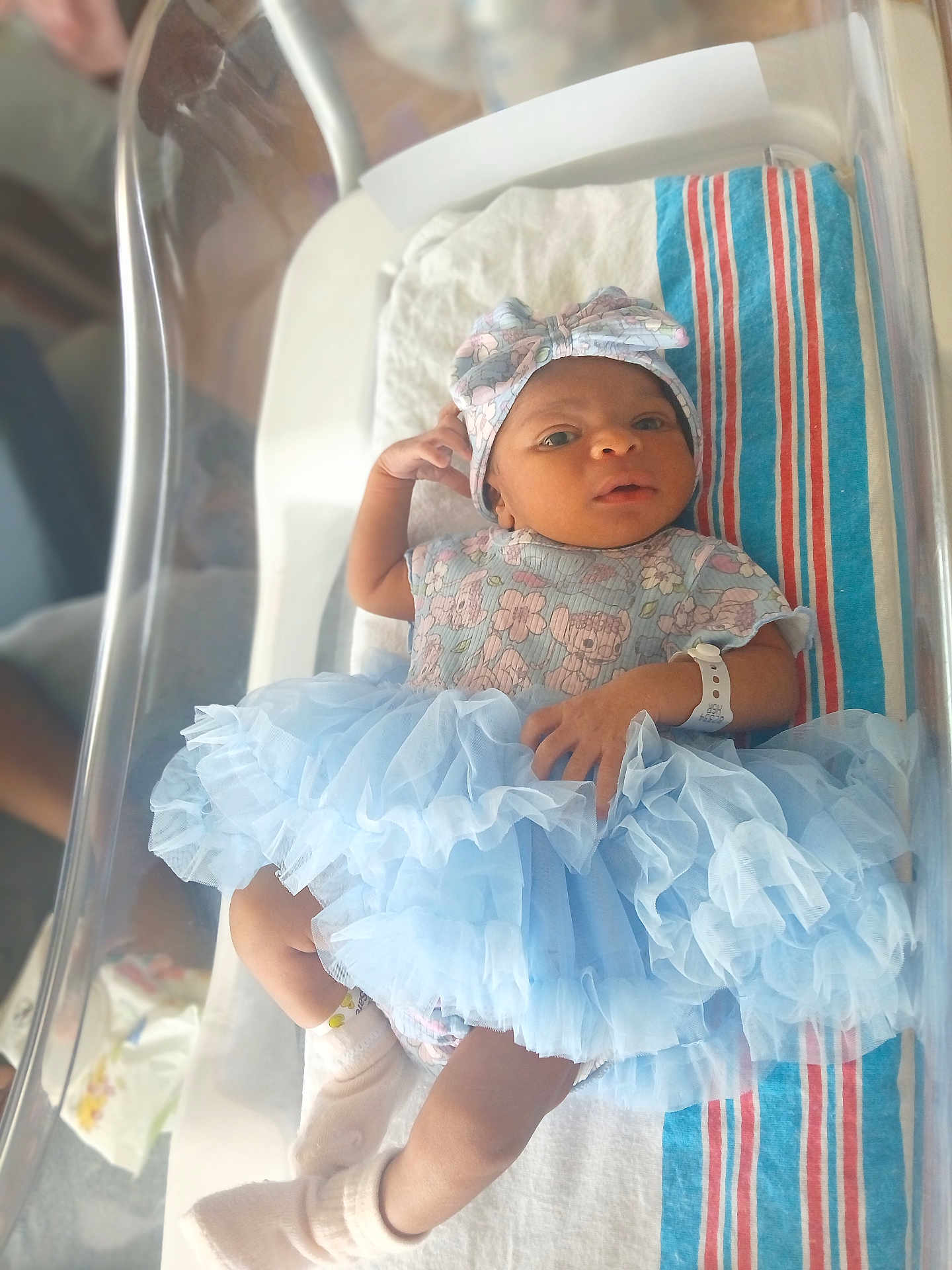 Zipporah is registered to the contest to win money with this photo: newborn, baby, infant, hospital, bassinet, tutu, headband, wristsband, blanket, clothing, sock, person, cute, portrait, laying_down, soft_light, hospital_bed, newborn_baby, baby_clothes, indoor