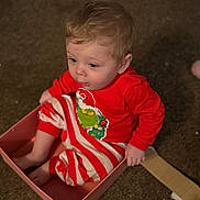 Freddie is registered to the contest to win money with this photo: toddler, child, baby, box, carpet, indoor, red_clothing, striped_pants, grinch, curly_hair, sitting, cute, small_box, floor, young_child, expression, playful, home, festive, person