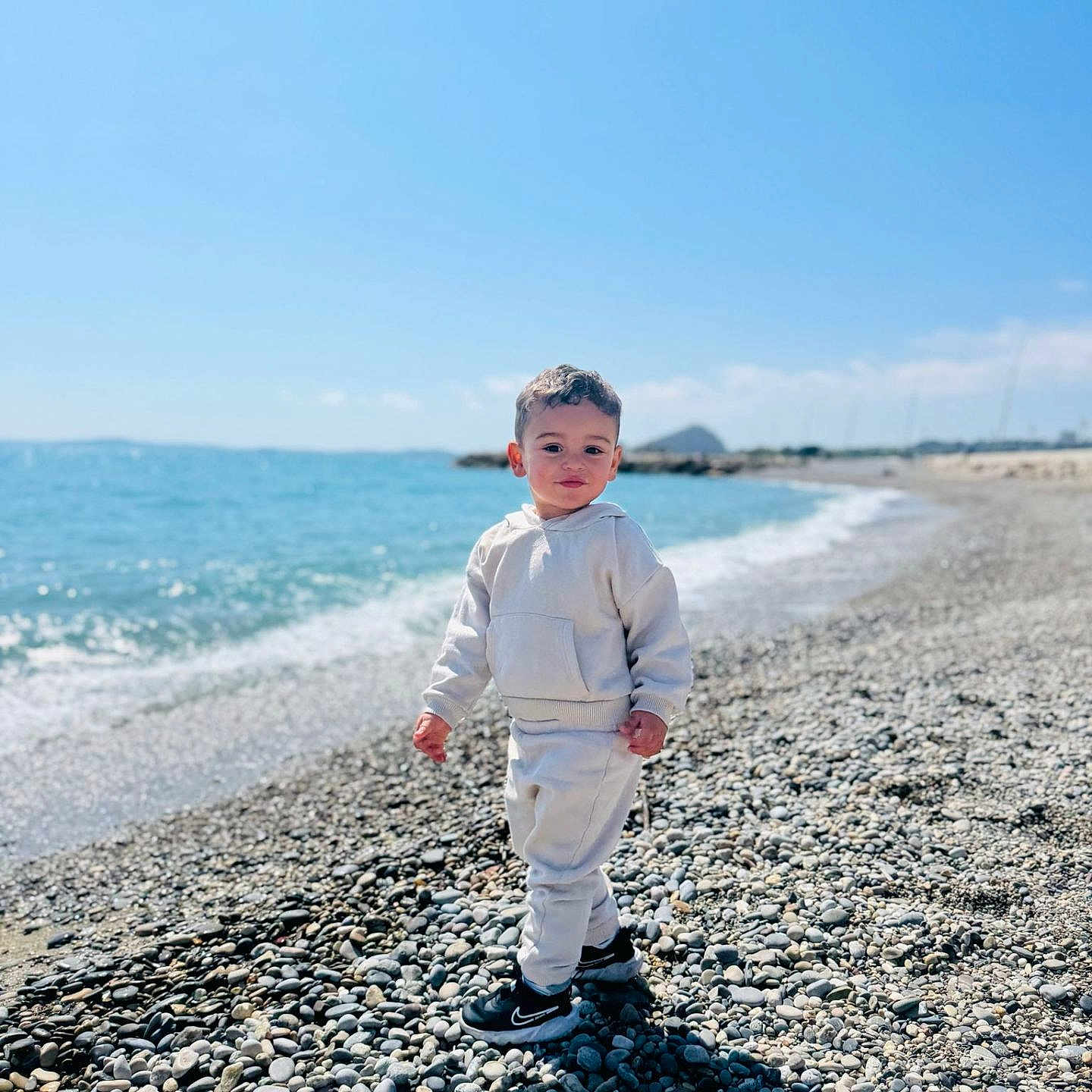 Kinen participe au concours pour gagner de l'argent avec cette photo : beach, casual, child, clothing, curious, daylight, hoodie, nature, outdoor, pants, pebbles, person, portrait, sea, shoes, sky, standing, sunny, toddler, water