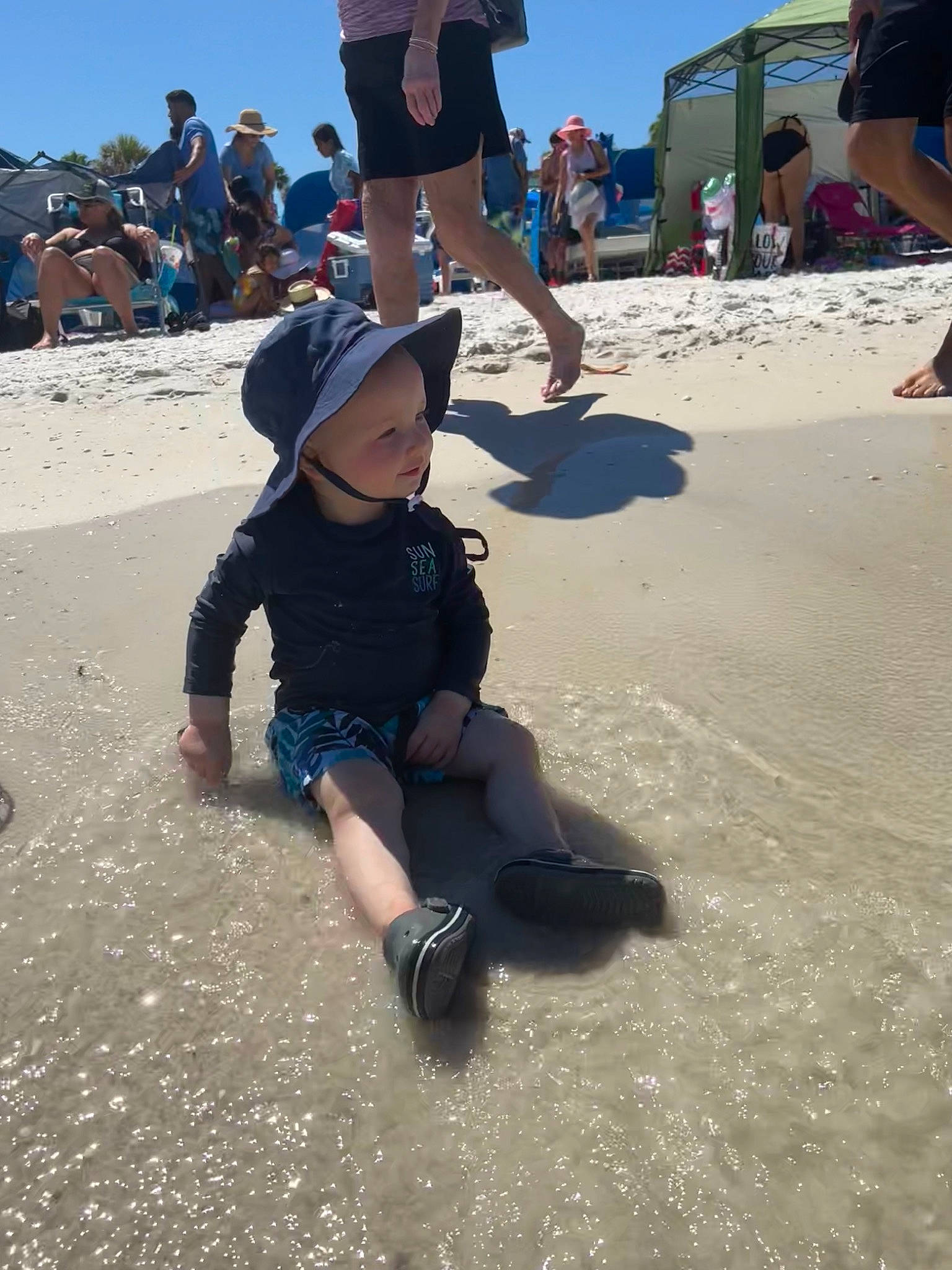 Eliott is registered to the contest to win money with this photo: baseball_cap, beach, body_of_water, fun, hat, headwear, landscape, leg, leisure, people_on_beach, person, recreation, sand, shadow, shorts, singing_sand, sky, sun_hat, toddler, tourism