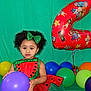 toddler, child, balloon, birthday, costume, watermelon, party, green_background, number_two, purple_balloon, red_balloon, curly_hair, headband, smiling, celebration, colorful, decorations, festive, cute, indoors