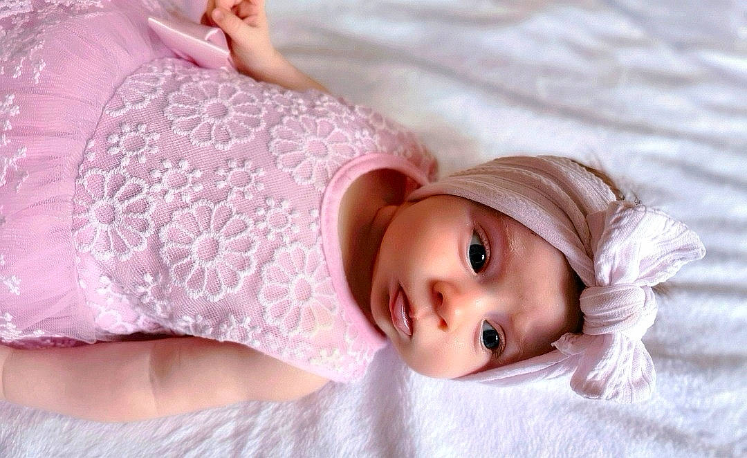 Célia participe au concours pour gagner de l'argent avec cette photo : baby, child, doll, dress, eye, eyelash, fashion_accessory, hair_accessory, head, headgear, headpiece, headwear, human_body, joint, linens, lip, person, pink, skin, sleeve