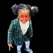 Zoe is registered to the contest to win money with this photo: child, girl, smiling, glasses, sunglasses, heart_shaped, hair_ties, plaid_blazer, white_tights, sandals, fashion, portrait, cute, happy, standing, jewelry, necklace, black_background, playful, confident