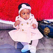 Zoe joined the competition — help win amazing prizes! accessory, baby, child, clothing, couch, cozy, cute, fashion, footwear, handbag, headband, indoor, infant, lion_emblem, person, pink_coat, portrait, red_fur, sitting, young_child