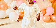 Zoe is registered to the contest to win money with this photo: balloons, blue_bow, carpet, celebration, child, cute, happy, indoor, orange, party_decorations, person, pink, pink_sunglasses, smiling, sneakers, standing, tiara, toddler, white, white_dress