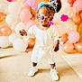 toddler, child, white_dress, sneakers, pink_sunglasses, tiara, blue_bow, balloons, party_decorations, pink, white, orange, carpet, indoor, celebration, smiling, standing, cute, happy, person
