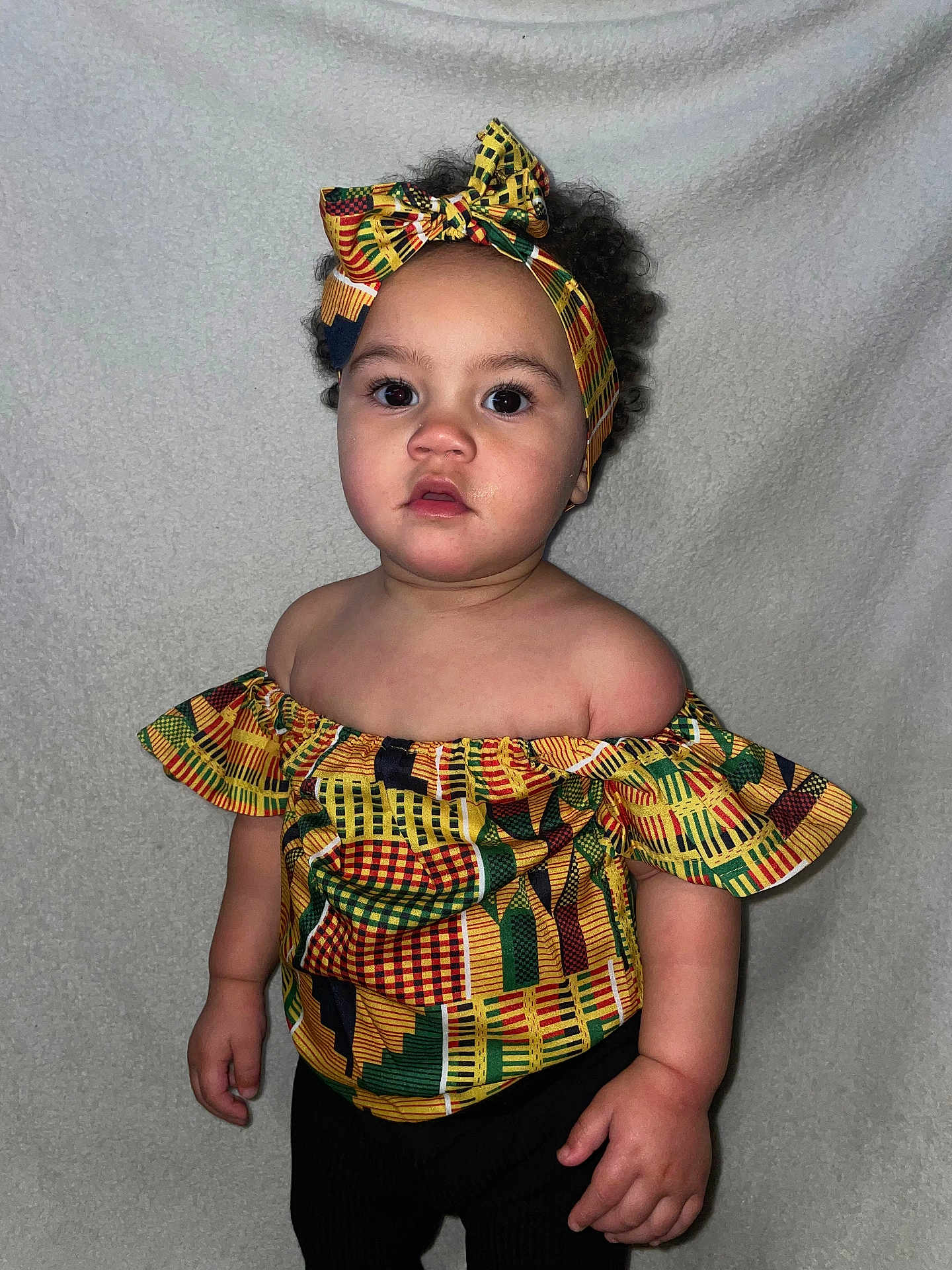 Emy participe au concours pour gagner de l'argent avec cette photo : toddler, child, headband, colorful_clothing, off_shoulder_top, curly_hair, portrait, indoor, neutral_background, cute, fashion, standing, young_child, face, big_eyes, expression, person, skin, hands, casual