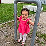 toddler, child, pink_dress, white_leggings, sandals, metal_pole, outdoor, grass, gravel, concrete_blocks, curly_hair, playground, person, standing, nature, greenery, summer, casual, young_child, daylight