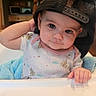 baby, child, high_chair, black_cap, mesh_cap, curious_look, indoor, kitchen, blue_blanket, infant, cute, portrait, casual_clothing, hand, face, person, toddlers, smiling, seated, home