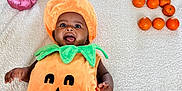 Genevieve is registered to the contest to win money with this photo: baby, pumpkin_costume, blanket, orange, decorative_pumpkin, smiling, face, child, holiday, fall, autumn, cute, happy, indoors, plush, costume, celebration, person, toddler, floor
