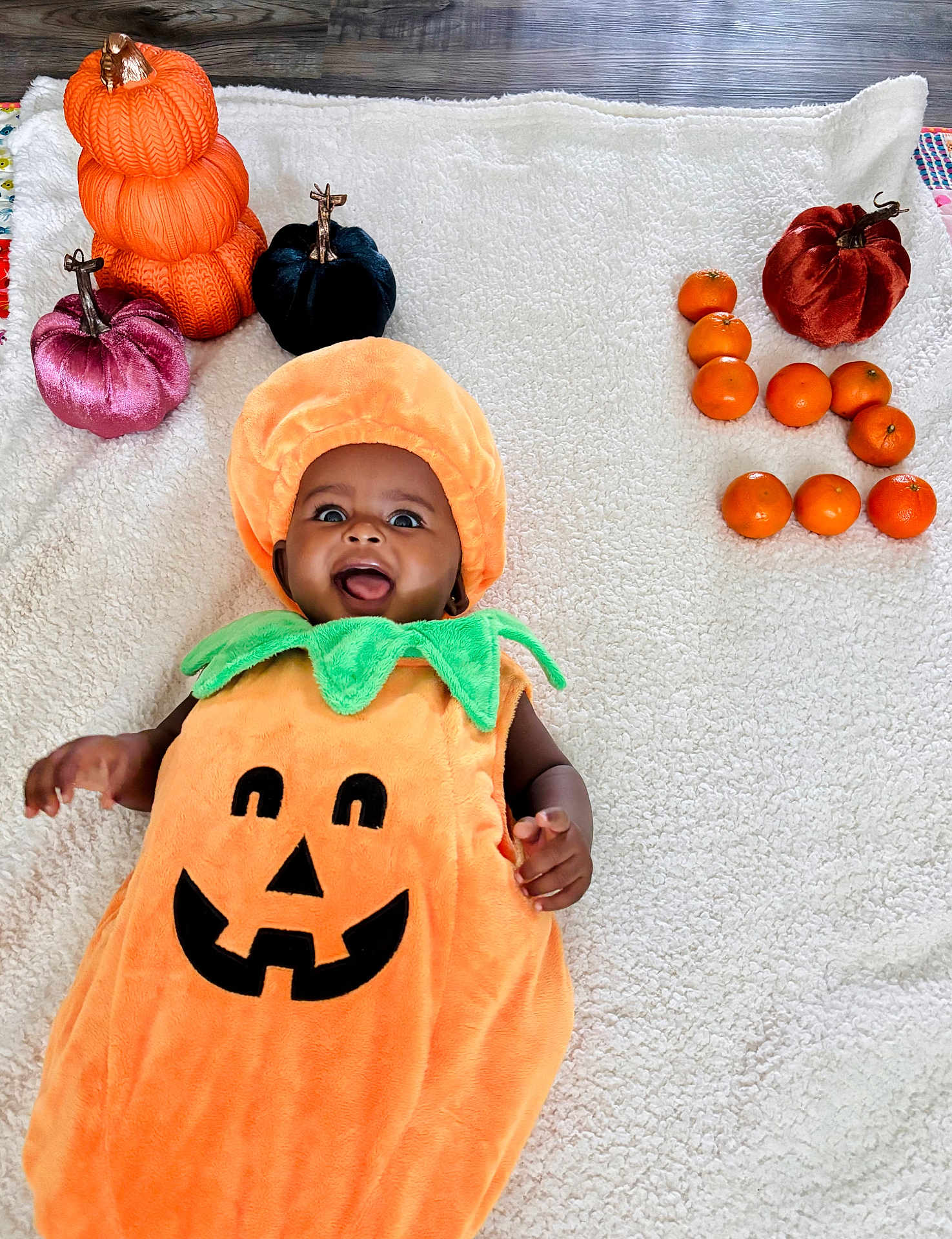 Genevieve is registered to the contest to win money with this photo: baby, pumpkin_costume, blanket, orange, decorative_pumpkin, smiling, face, child, holiday, fall, autumn, cute, happy, indoors, plush, costume, celebration, person, toddler, floor