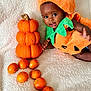 Genevieve is registered to the contest to win money with this photo: baby, child, pumpkin_costume, orange, knitted_pumpkin, fruit, blanket, cute, smiling, portrait, indoors, soft_texture, autumn, holiday, festive, toddler, playful, colorful, happy, person