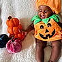 baby, child, pumpkin_costume, orange, green, smiling, happy, sitting, blanket, decorative_pumpkins, plush, cute, holiday, autumn, festive, indoors, soft_texture, infant, joyful, portrait