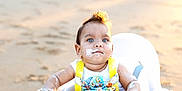 Marcello is registered to the contest to win money with this photo: baby, child, high_chair, beach, sand, sunlight, frosting, food, messy, blue_eyes, outdoor, summer, cute, infant, person, sitting, sunset, playful, yellow_straps, white_clothing