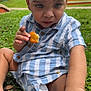toddler, child, grass, outdoor, food, snack, striped_clothing, blue, white, baby, sitting, hand, face, expression, park, nature, daylight, person, young_child, casual