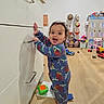 toddler, child, pajamas, standing, kitchen, cabinet, floor, toy, dollhouse, playroom, happy, curious, indoor, wooden_floor, person, smiling, furniture, home, colorful, young_child