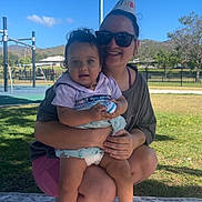 Leearnah joined the competition — help win amazing prizes! baby, child, parent, adult, outdoor, playground, birthday, party_hat, smiling, sitting, holding_toy, toy_keyboard, maraca, blanket, grass, sunny, blue_sky, playground_equipment, portrait, family
