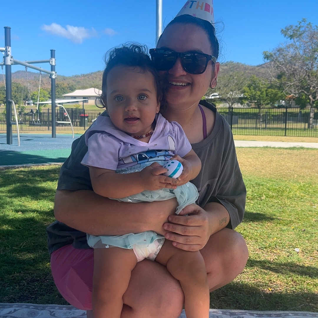 Leearnah joined the competition — help win amazing prizes! baby, child, parent, adult, outdoor, playground, birthday, party_hat, smiling, sitting, holding_toy, toy_keyboard, maraca, blanket, grass, sunny, blue_sky, playground_equipment, portrait, family