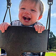 Joshua is registered to the contest to win money with this photo: baby, child, face, grass, gripping, hands, happy, laughing, outdoor, park, playground, playground_equipment, portrait, seated, sky, smiling, sunny, swing, teeth, toddler