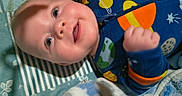 Buddy is registered to the contest to win money with this photo: baby, bedding, blanket, cheerful, close_up, cozy, eyes, face, fist, hand, infant, lying_down, onesie, pajamas, planet, smiling, soft_texture, space_pattern, stars, zipper