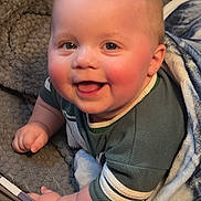 Buddy is registered to the contest to win money with this photo: baby, blanket, blue, cheeks, child, clothing, colorful, cute, face, green, happy, indoor, infant, person, playpen, portrait, smiling, soft_texture, toddler, toy