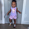 child, cute, door, floor, hair_up, happy, hello_kitty, home, indoor, mismatched_socks, person, playful, power_outlet, purple_clothing, shorts, sleeveless_shirt, smiling, standing, toddler, wall