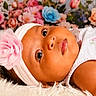 baby, infant, headband, flower, pink, white_dress, curly_hair, fluffy_rug, portrait, closeup, face, large_eyes, flower_background, soft_texture, cute, child, indoors, resting, beautiful, adorable