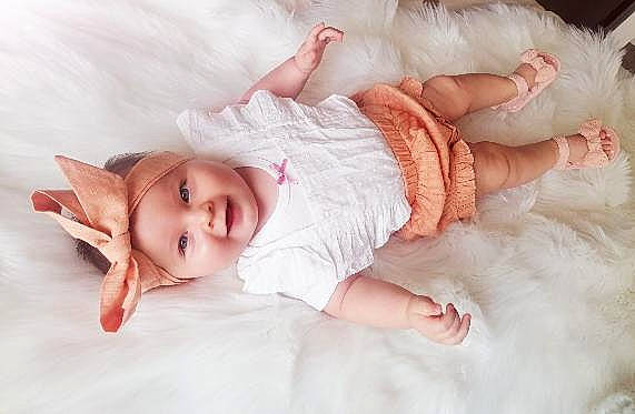 Lyana participe au concours pour gagner de l'argent avec cette photo : baby, baby_toddler_clothing, child, comfort, dress, eye, face, facial_expression, finger, hand, happy, headgear, headwear, human_body, iris, linens, person, pink, skin, sleeve