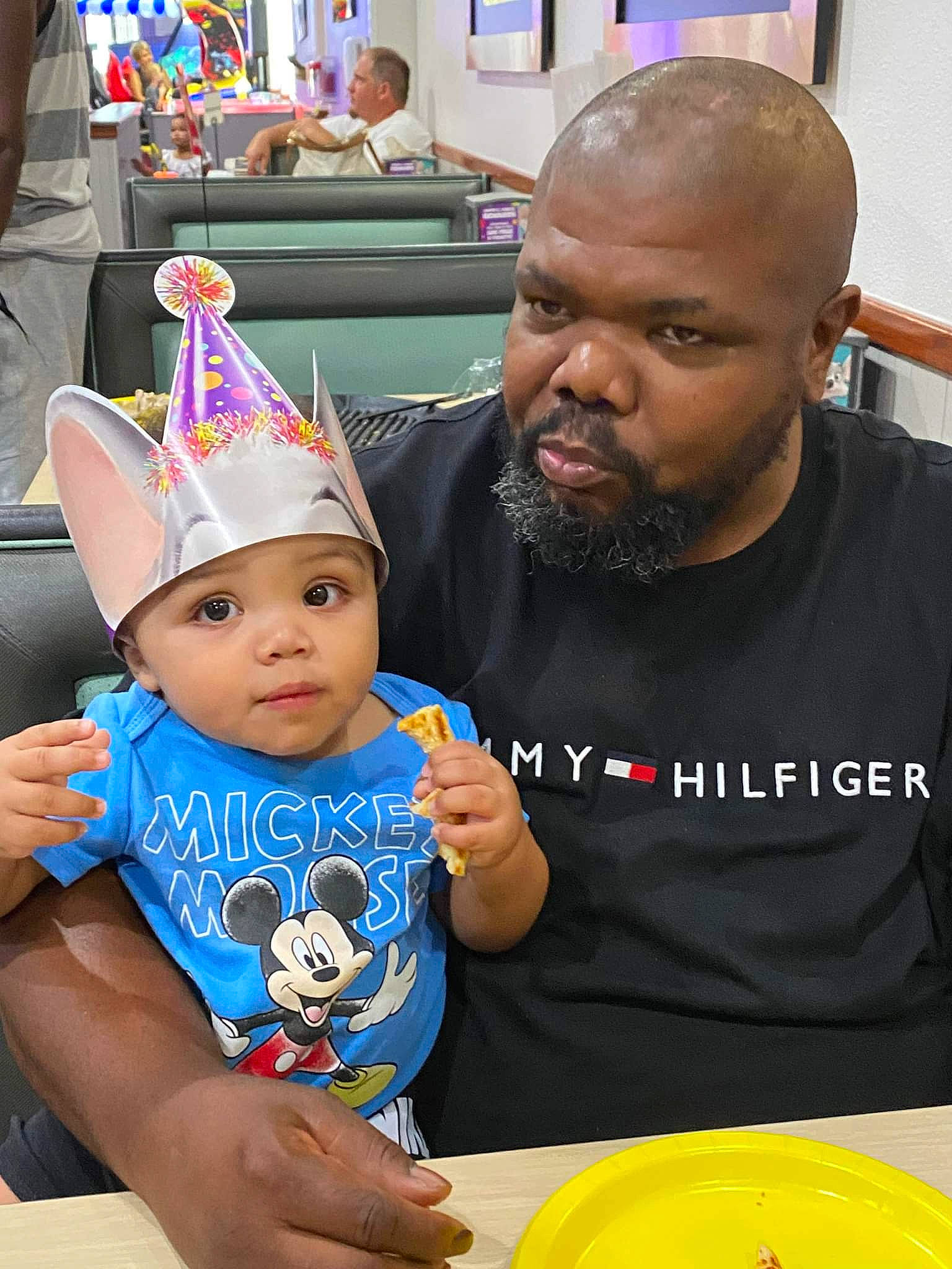 Kendrick is registered to the contest to win money with this photo: baby, beard, birthday, cap, chair, child, costume_hat, event, fashion_accessory, fun, happy, headwear, leisure, party_hat, party_supply, person, plate, sharing, t_shirt, tableware