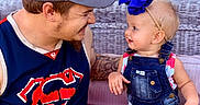 Amirah is registered to the contest to win money with this photo: adult, baby, blue_bow, cap, casual_clothing, child, cute, denim_overalls, face, family, happy, hat, interaction, man, outdoor, people, portrait, smiling, tattoo, wicker_couch