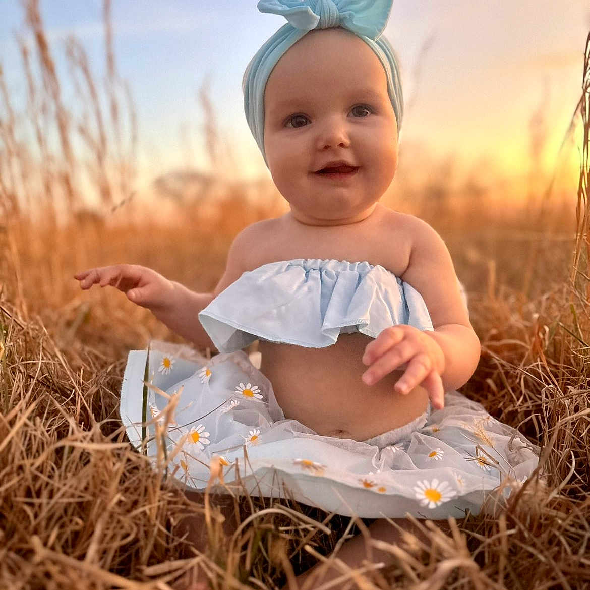 Amirah is registered to the contest to win money with this photo: baby, child, field, grass, sunset, outdoor, nature, headband, dress, blue, smiling, sitting, happy, portrait, daisy, flower_pattern, sunlight, warm_light, cute, infant