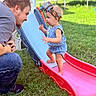 Amirah joined the competition — help win amazing prizes! toddler, child, man, slide, playground, outdoor, grass, toy, headband, blue_clothing, interaction, smile, baby, summer, family, playtime, fun, parent, leisure, sunlight