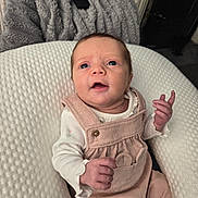 Lottie-May joined the competition — help win amazing prizes! baby, infant, child, overalls, pink_clothing, white_shirt, cushion, blanket, remote_control, indoor, person, face, hand, sitting, expression, young_child, texture, cozy, curious, portrait