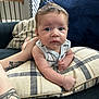 baby, infant, pillow, couch, tattoo, arm, face, eyes, hair, plaid, striped_clothing, indoor, person, child, cute, expression, skin, furniture, relaxing, home