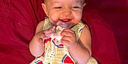 Bella is registered to the contest to win money with this photo: baby, smiling, pacifier, yellow_top, watermelon_print, black_pants, red_blanket, happy, child, infant, cute, lying_down, hands, face, portrait, indoors, skin, head, clothing, person