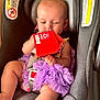 baby, child, car_seat, purple_dress, red_carton, warning_label, seatbelt, infant, curious, indoor, sitting, soft_toys, clothing, face, head, hand, foot, safety, seat, closeup