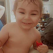 Ares is registered to the contest to win money with this photo: toddler, child, smile, indoor, toy, red, face, skin, hair, hand, person, happy, living_room, couch, furniture, background, casual, cute, expression, relaxed