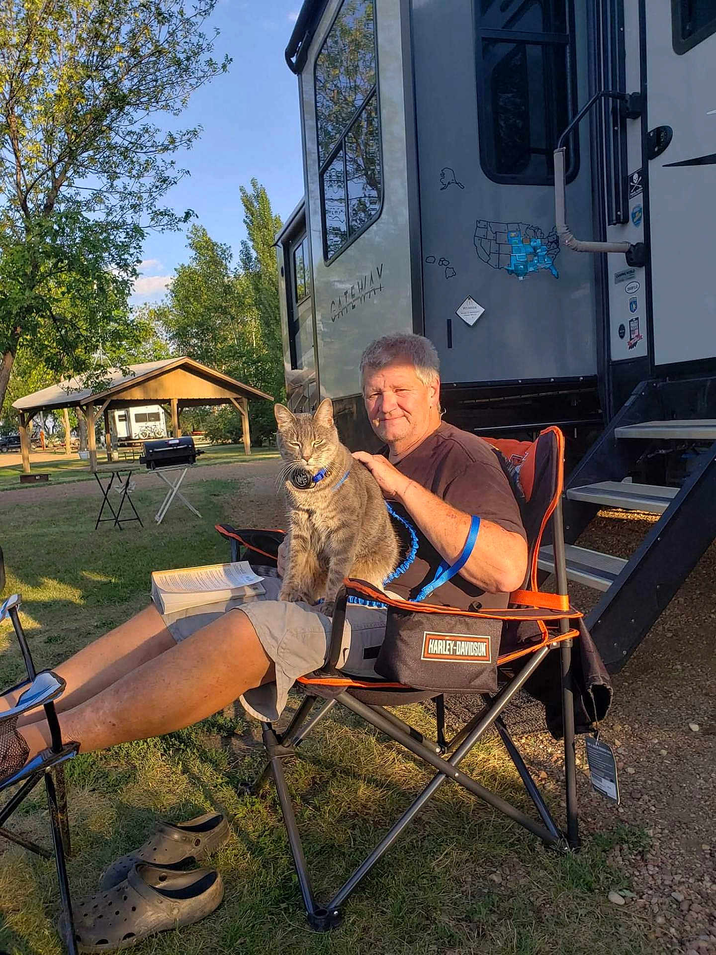 Smoky Veverka joined the competition — help win amazing prizes! man, cat, camping_chair, rv, outdoor, grass, tree, pavilion, sunlight, book, shoes, harley_davidson, leisure, pet, relaxation, nature, summer, daylight, animal, person