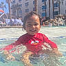 blue_sky, child, daytime, elmo, fun, happy, hotel, lounge_chairs, outdoor, palm_trees, people, pool, red_shirt, smiling, splash, summer, sunny, swimming, vacation, water
