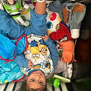 Thomas is registered to the contest to win money with this photo: bed, blanket, blue_clothing, buzz_lightyear, child, colorful, crib, curly_hair, cute, indoors, minions, person, playful, smiling, socks, soft_toy, spiderman, stuffed_animal, toddler, toy