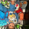 bed, blanket, blue_clothing, buzz_lightyear, child, colorful, crib, curly_hair, cute, indoors, minions, person, playful, smiling, socks, soft_toy, spiderman, stuffed_animal, toddler, toy