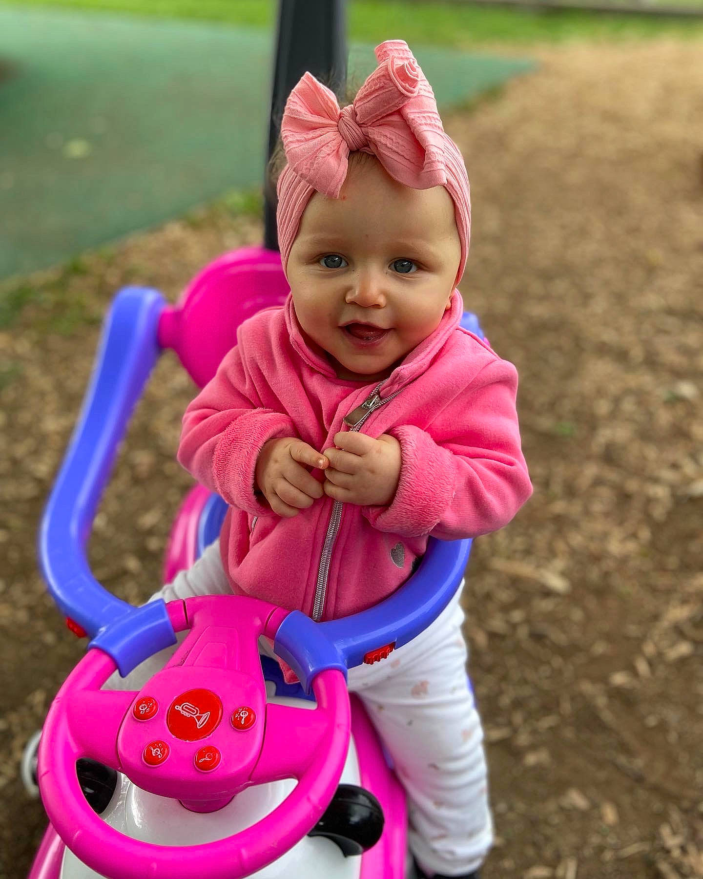 Sofia participe au concours pour gagner de l'argent avec cette photo : baby, baby_toddler_clothing, eye, face, grass, hand, happy, headwear, human_body, people_in_nature, person, pink, purple, red, riding_toy, skin, smile, tire, toddler, vehicle