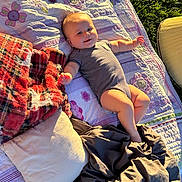 Bruce is registered to the contest to win money with this photo: baby, infant, quilt, blanket, pillow, outdoor, grass, sunlight, smiling, clothing, striped_onesie, relaxing, child, cute, happy, lying_down, soft_texture, warm_light, resting, nature