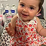 baby, child, smiling, dress, hair_clip, indoor, leopard_print, blanket, bottle, skincare, face, sitting, cute, person, infant, pink, pattern, happy, young_child, closeup