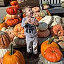 child, pumpkin, pumpkin_patch, outdoor, fall, autumn, bench, smiling, clothing, person, daylight, nature, harvest, fun, stacked_pumpkins, casual_wear, holiday, seasonal, playful, young