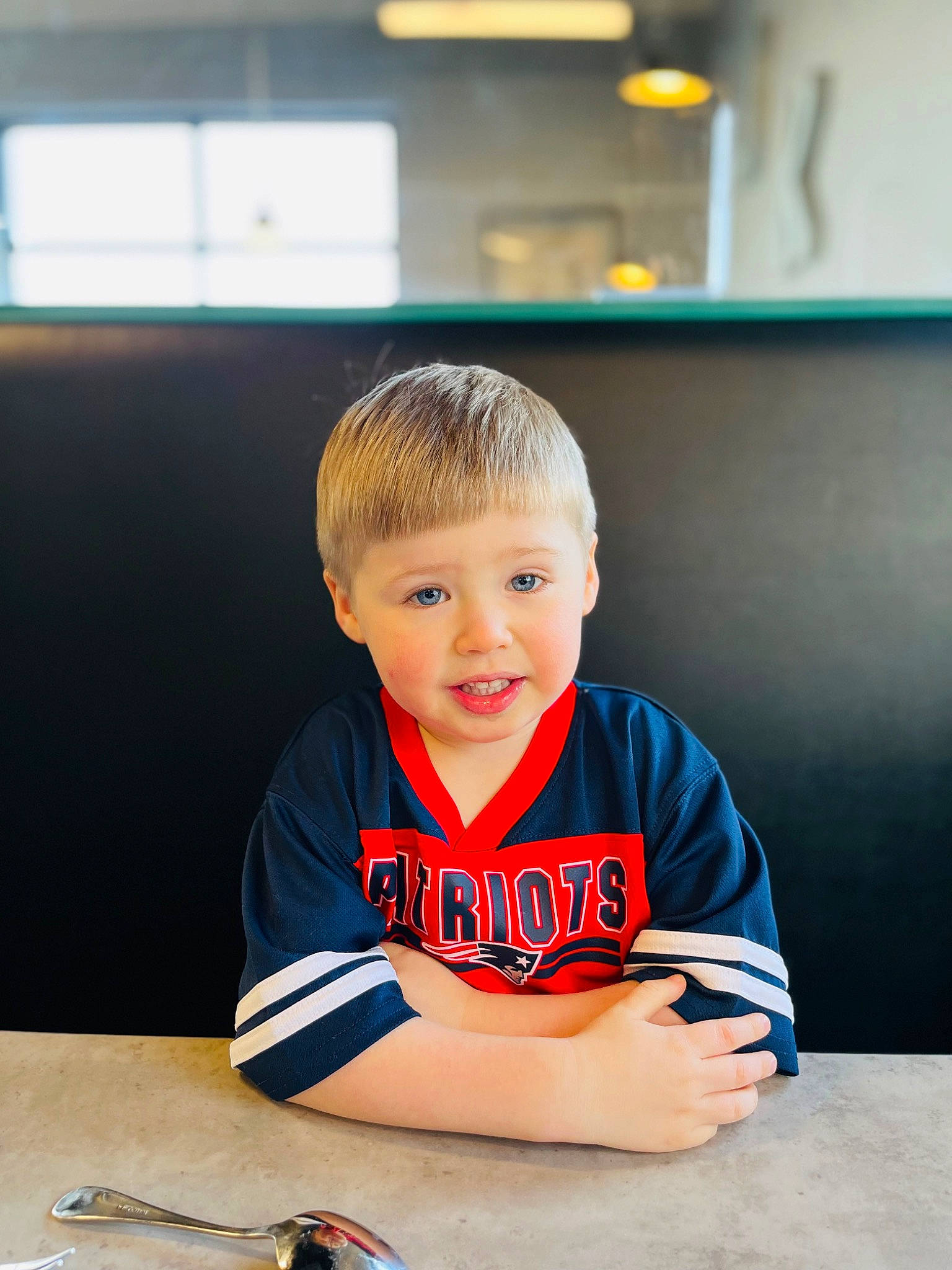 Maverick is registered to the contest to win money with this photo: carmine, chair, child, desk, flooring, fun, hairstyle, happy, hardwood, pen, person, room, sitting, sleeve, smile, sportswear, standing, t_shirt, table, toddler