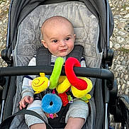 Jordan joined the competition — help win amazing prizes! baby, child, stroller, plush_toy, colorful_toy, outdoor, cobblestone, infant, clothing, seat, straps, cute, person, portrait, happy, smile, head, hand, feet, fabric